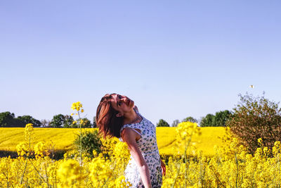 Beautiful woman standing on yellow flower field against clear sky