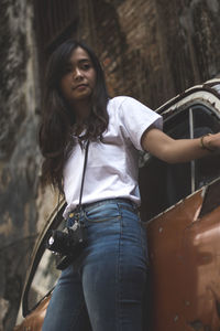 Low angle view of young woman smiling while standing by abandoned car