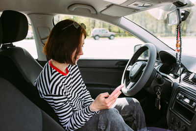 Portrait of a young brunette woman driving in a car using a smartphone