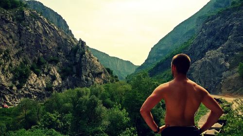 Rear view of shirtless man standing on mountain against clear sky