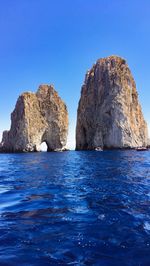 Rock formations in sea against clear blue sky