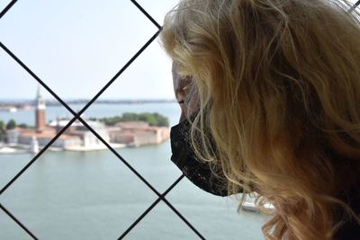 Woman with protective face mask looking away through window fence