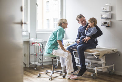 Side view of smiling female doctor talking to boy with father in clinic