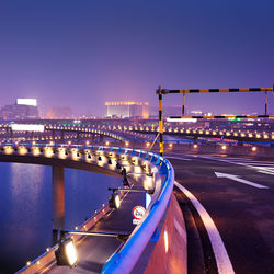 Light trails on bridge in city against sky at night