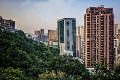 Buildings in city by trees against sky