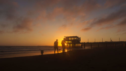 Silhouette people standing on beach against sky during sunset