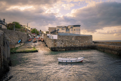 Nautical vessel on sea by buildings against sky during sunset