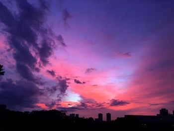 Silhouette of city against cloudy sky during sunset