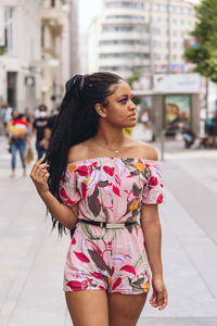 Young woman looking away while standing on street in city