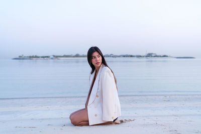 Beautiful middle eastern woman sitting on the beach wearing jacket