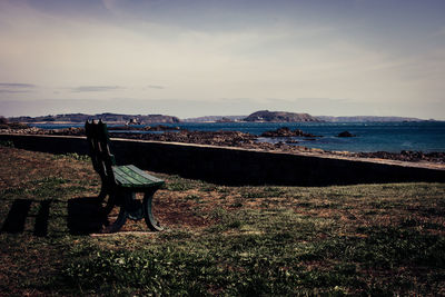 Man on bench by sea against sky