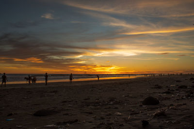 People on beach against sky during sunset