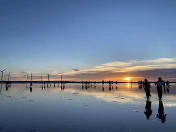 Silhouette people on beach against sky during sunset