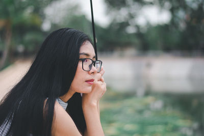 Side view of thoughtful young woman holding umbrella looking away while standing in park