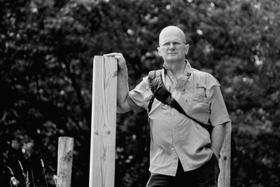 Front view of mature man standing by wooden post