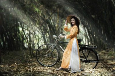 Side view of woman with bicycle standing in forest