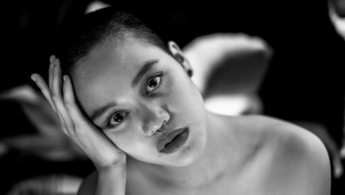 Close-up portrait of shirtless young woman with head in hand