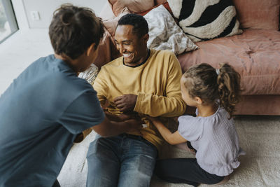 High angle view of happy father playing with kids while sitting near sofa in living room at home