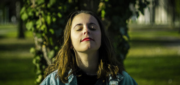 Close-up of young woman with eyes closed against plant