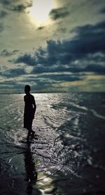 Silhouette man standing in sea against sky