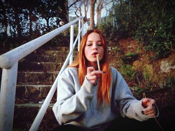 Woman blowing lit candle while sitting by railing