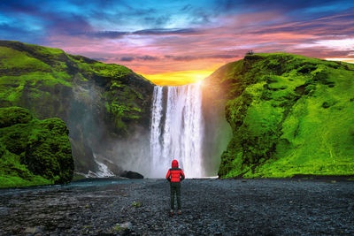 Rear view of man standing by waterfall against sky