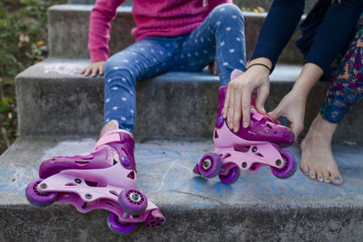Low section of mother assisting daughter in wearing roller skates while sitting on steps