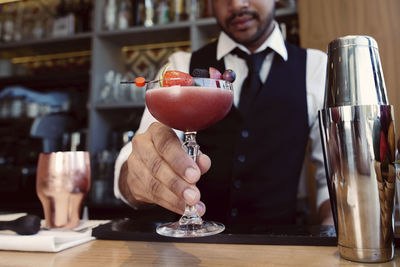 Bartender holding glass with cocktail at bar