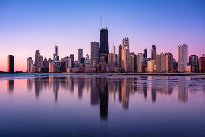 Reflection of buildings in city against sky during sunset