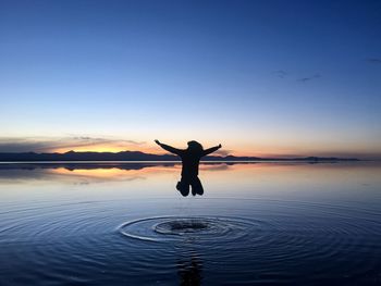 Rear view of silhouette person in lake against sky during sunset