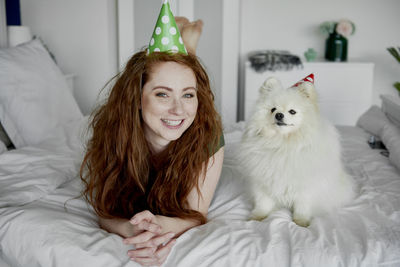 Portrait of smiling woman lying by dog on bed at home
