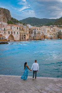 Rear view of people on sea by city against sky