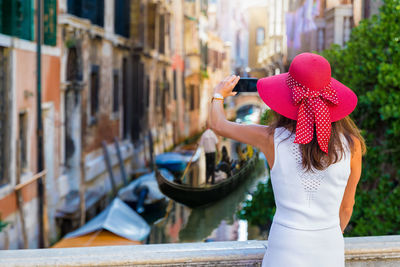 Rear view of woman photographing against canal in city