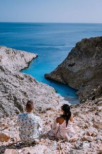 Rear view of couple standing on rock by sea against sky