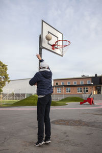 Rear view of teenage boy shooting basketball