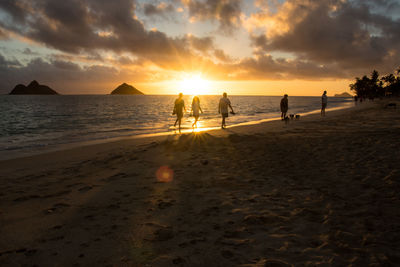 People at beach against sky during sunset