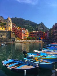 Boats moored in river by buildings against sky