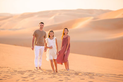 Full length of friends walking on sand