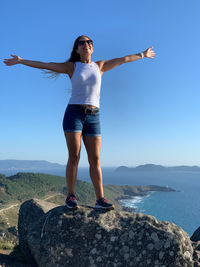 Full length of young woman standing on rock against sky