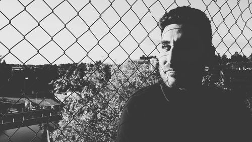 Man standing by chainlink fence against clear sky