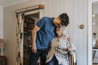 Happy male caregiver embracing senior woman at home