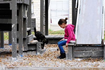 Side view full length of girl by tortoiseshell cat on wooden play equipment