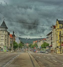 Road passing through city against cloudy sky