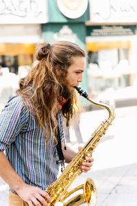 Profile of a young man with long hair playing saxophone in the street