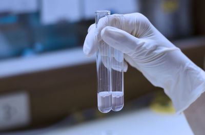 Cropped hand of scientist wearing surgical glove holding test tubes in laboratory