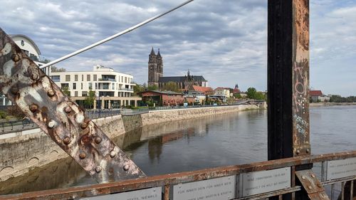 Bridge over river by buildings in city against sky