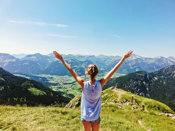 Rear view of young woman with arms raised standing on mountain against sky