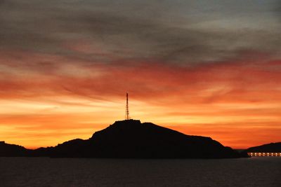 Silhouette tower by sea against orange sky