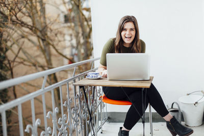 Cheerful young woman using laptop on the balcony