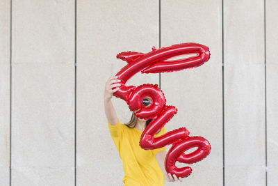 Portrait of woman holding balloons with text while standing against wall